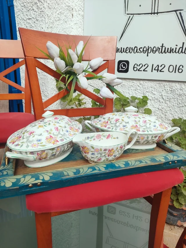 Vajilla Haddon Hall 1 La vajilla Haddon Hall, fabricada por la prestigiosa marca inglesa Minton y en algunos modelos por Royal Doulton, es una colección de porcelana fina decorada con motivos florales multicolores. Su diseño está inspirado en los jardines de la histórica mansión Haddon Hall, ubicada en Derbyshire, Inglaterra, lo que le confiere un aire romántico y atemporal. Las piezas suelen presentar un fondo blanco con ribetes verdes y una decoración de flores silvestres en tonos suaves, como rosas, lilas y azules, distribuidas con elegancia por toda la superficie. Esta vajilla se produce en porcelana de ceniza