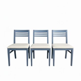 Sillas de madera pintadas en azul con respaldo vertical y asiento tapizado en blanco. Diseño clásico y cómodo.